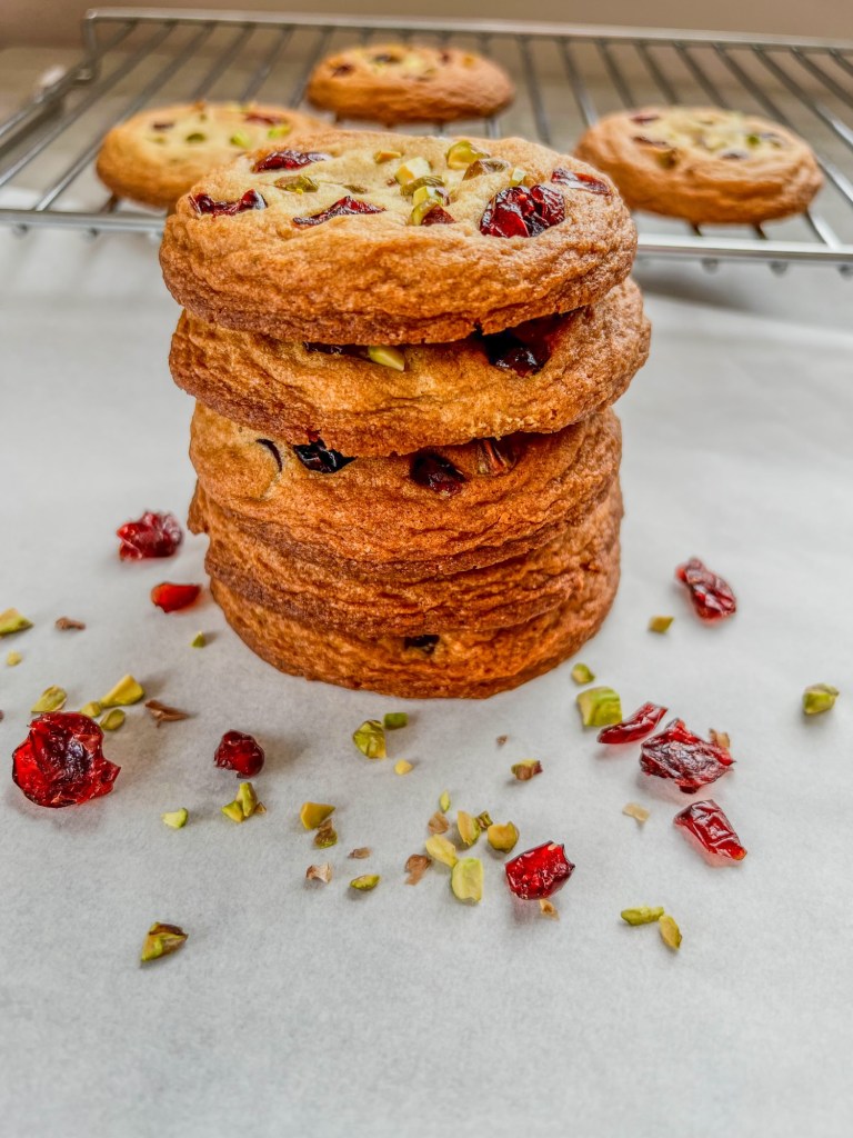 Orange cranberry pistachio cookies stacked up with some pistachios and cranberries scattered around