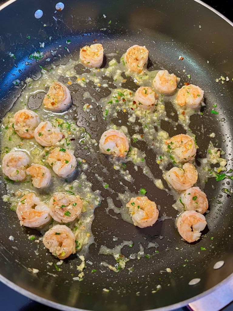 Shrimp being tossed in scampi sauce in a skillet on the stove