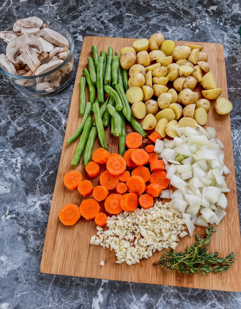 A bunch of veggies for stew cut up on a wooden cutting board 