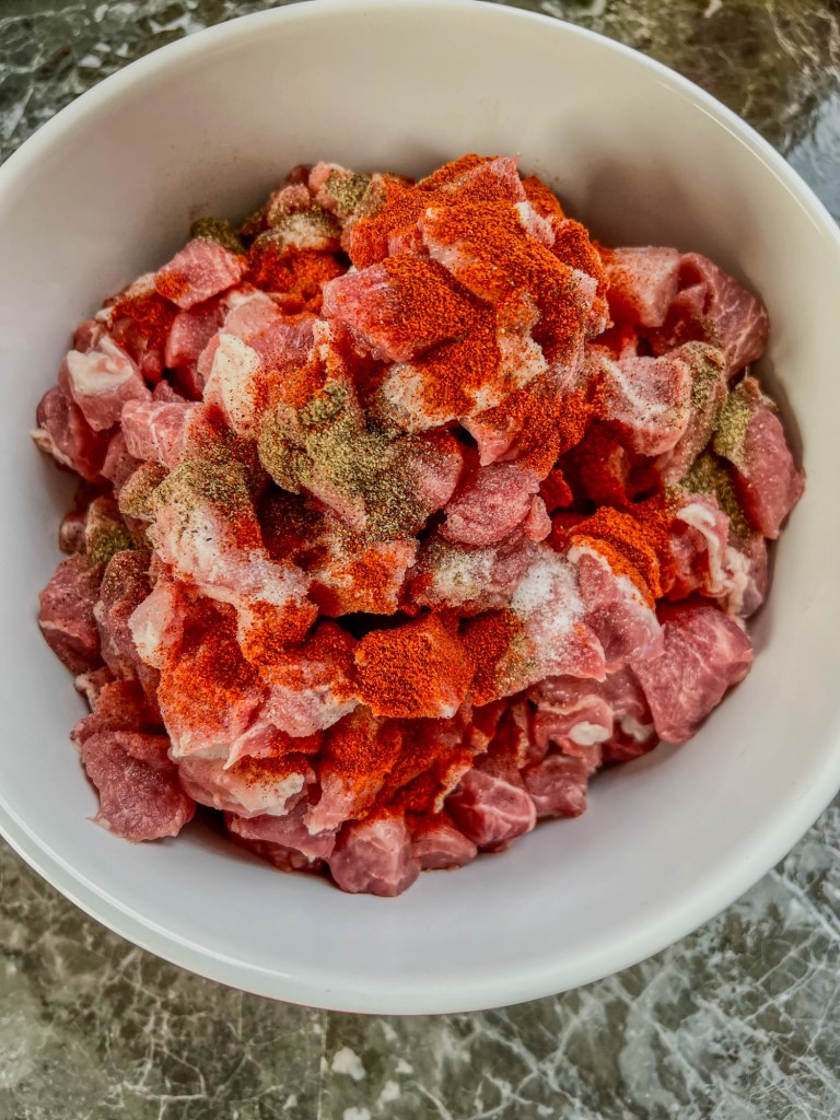 Pork cut into chunks in a large bowl with some seasonings sprinkled on