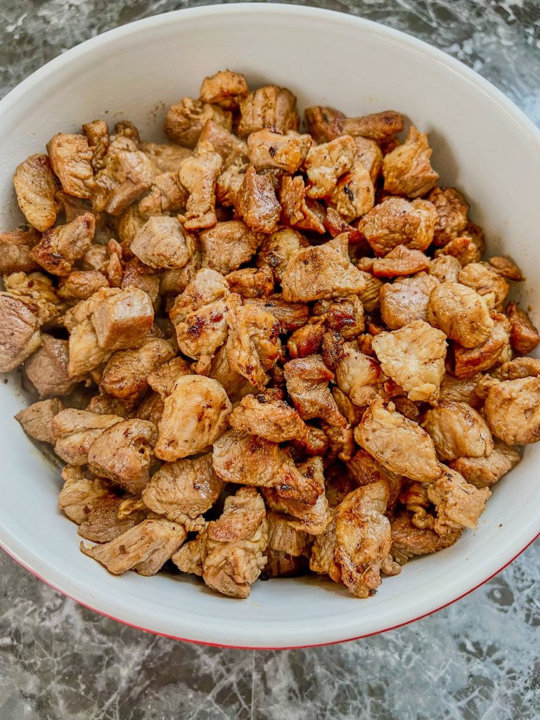 Pork cut into chunks that's been seared in a cast iron and moved to a large bowl