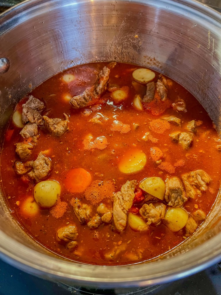 Tomato pork stew cooking in a large pot on the stove