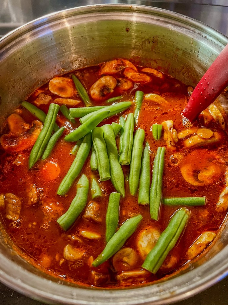 Stew cooking on the stove with some freshly added green beans
