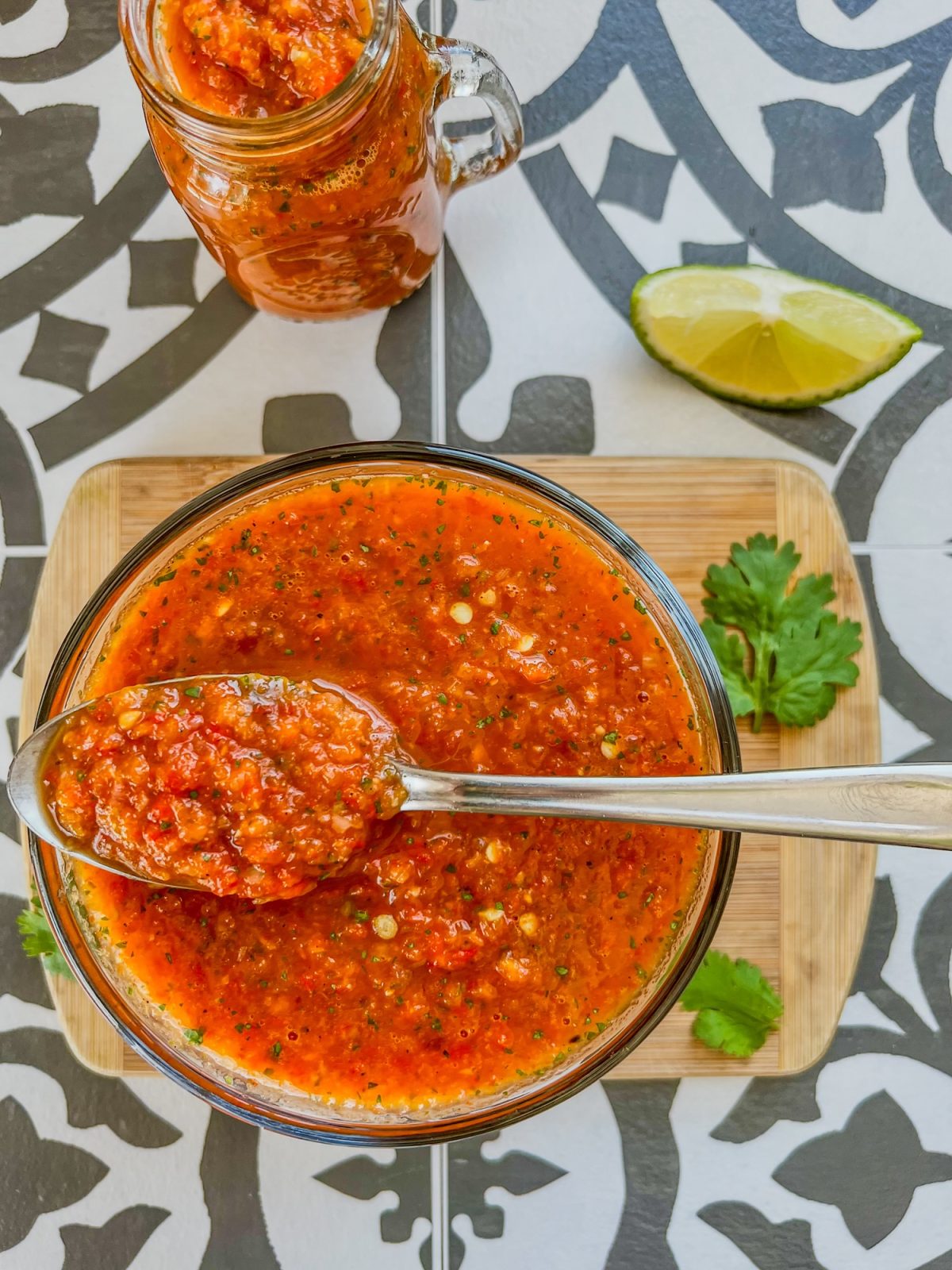 Homemade hot sauce in a dish with a spoon inside with some cilantro and lime on the side