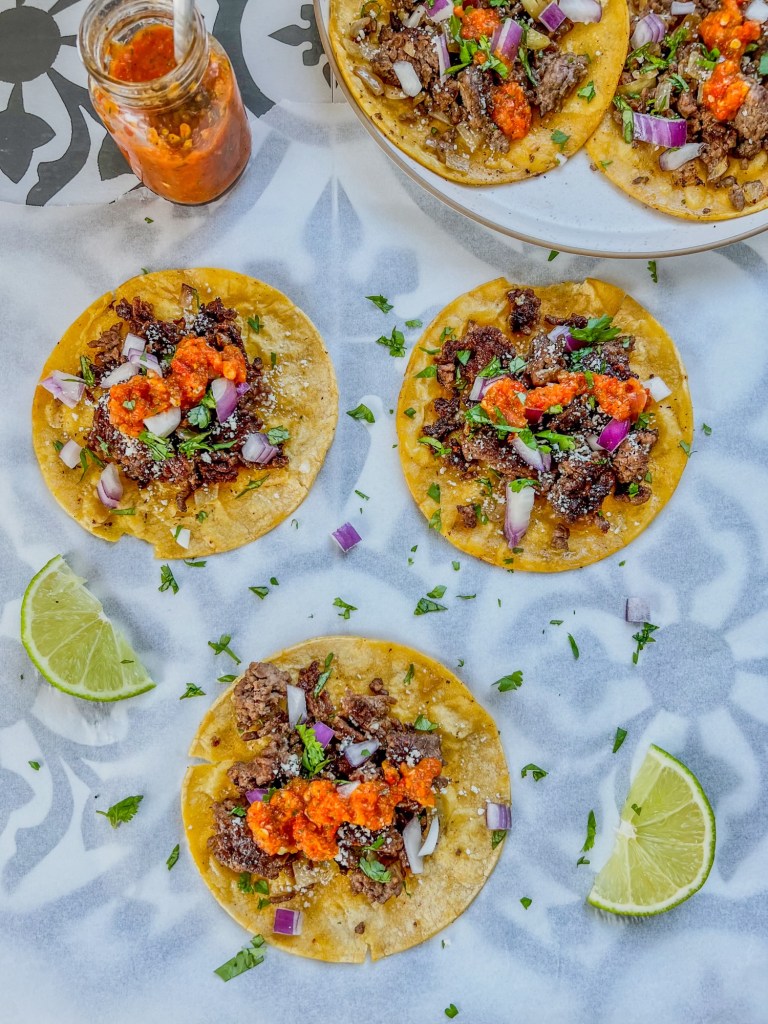 Crispy beef smash tacos with homemade hot sauce and garnishes all around on a countertop