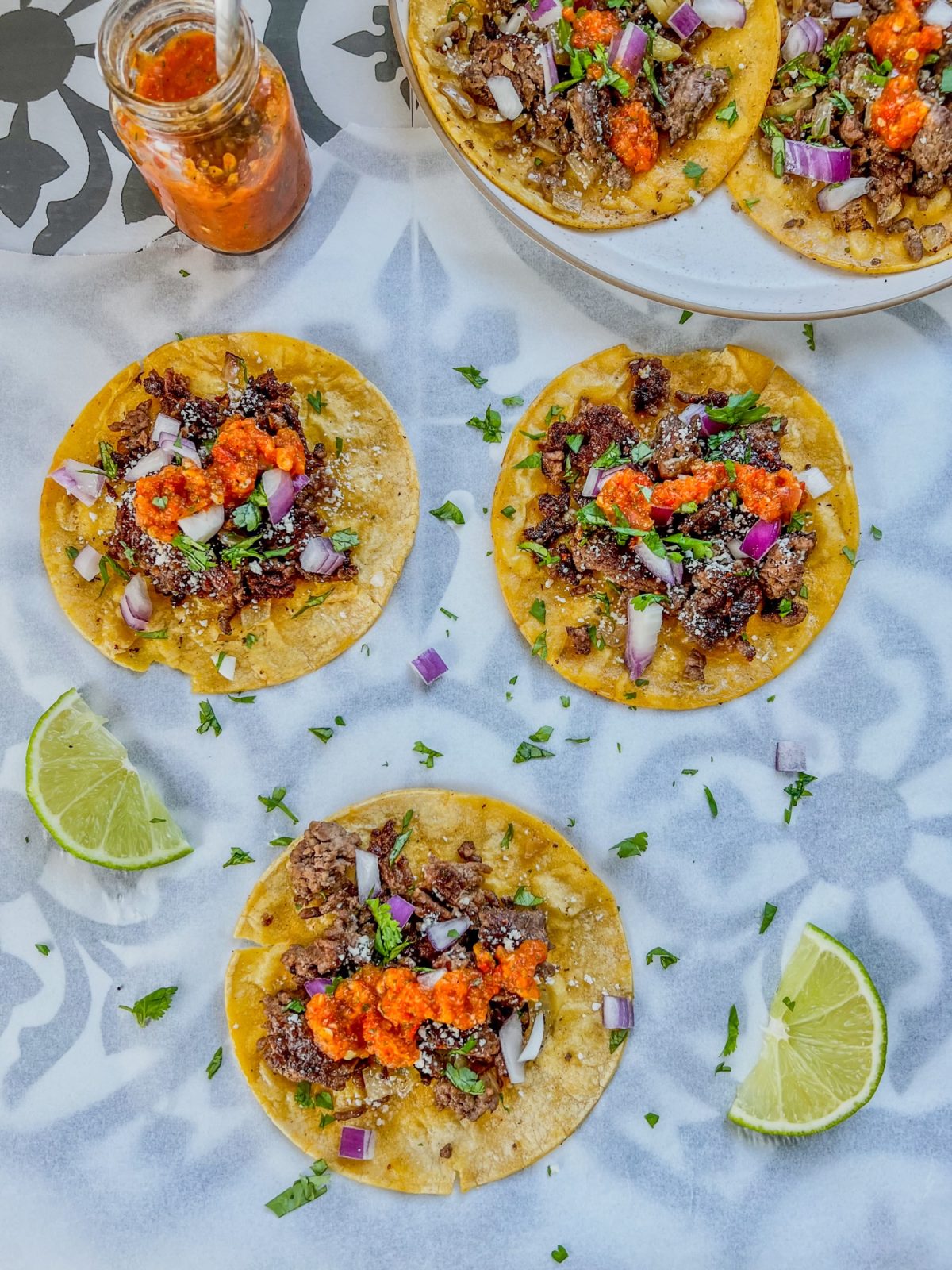 Crispy beef smash tacos on a countertop with lime, cilantro, and onion scattered around