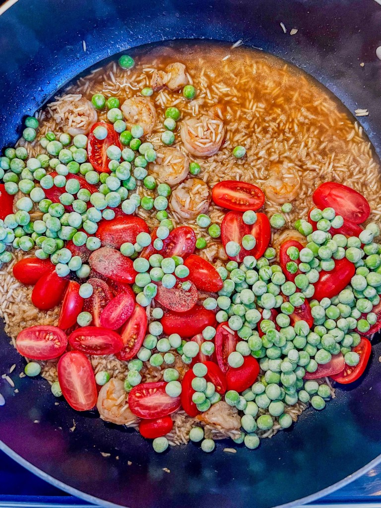 Shrimp fried rice being made in a skillet with some freshly added shrimp and peas