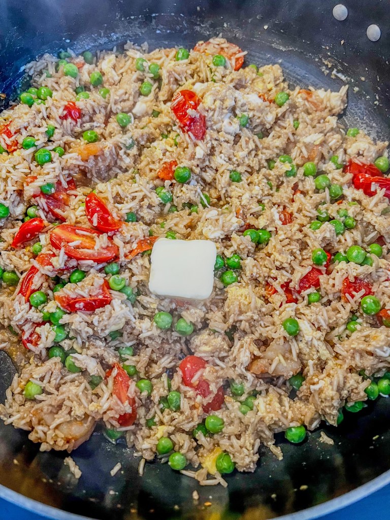 Shrimp fried rice cooking in a skillet on the stove with some fresh butter newly added