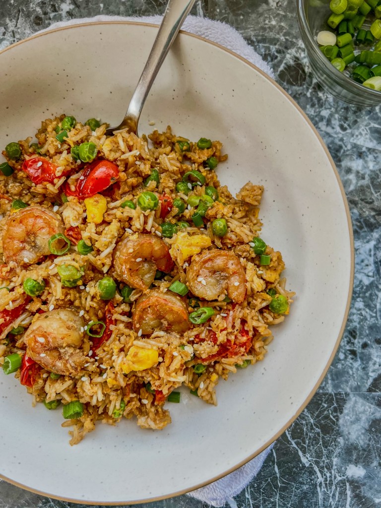 Shrimp fried rice in a white bowl with a spoon inside with a dish of green onions off to the side