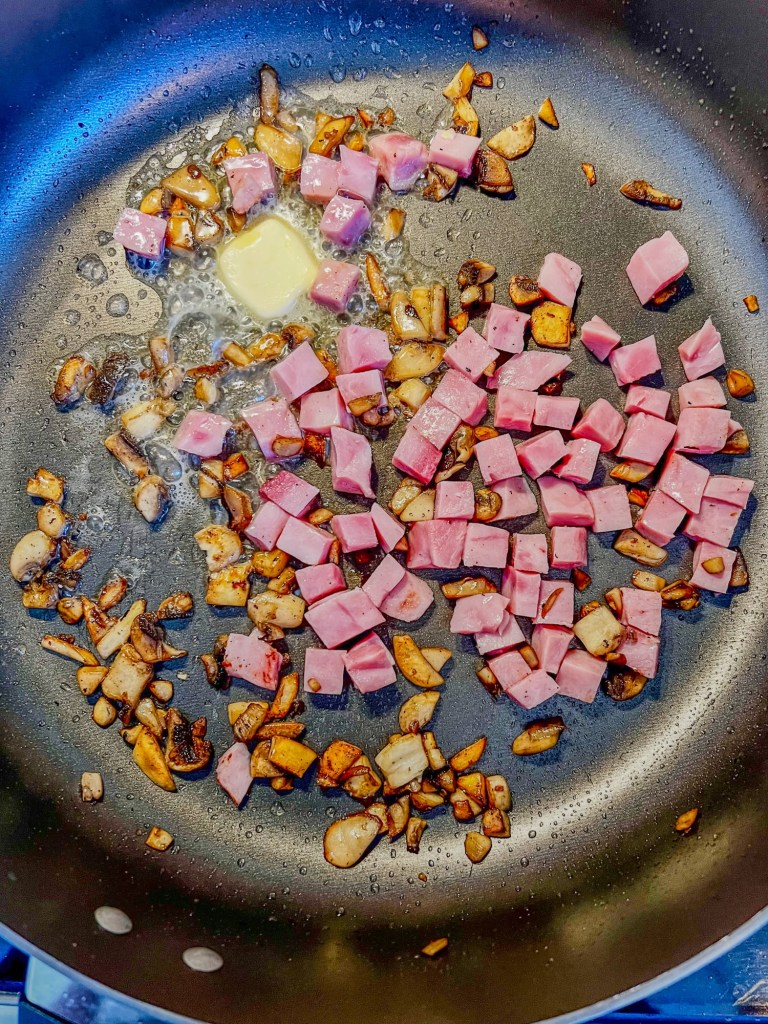 Mushrooms, ham, and butter cooking in a skillet