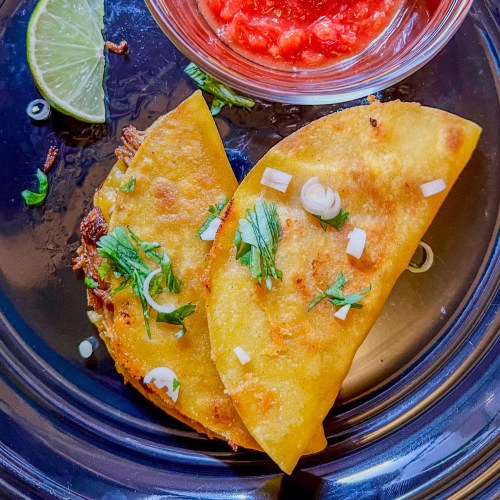Fried Pulled Pork Tacos on a black plate with a side of salsa