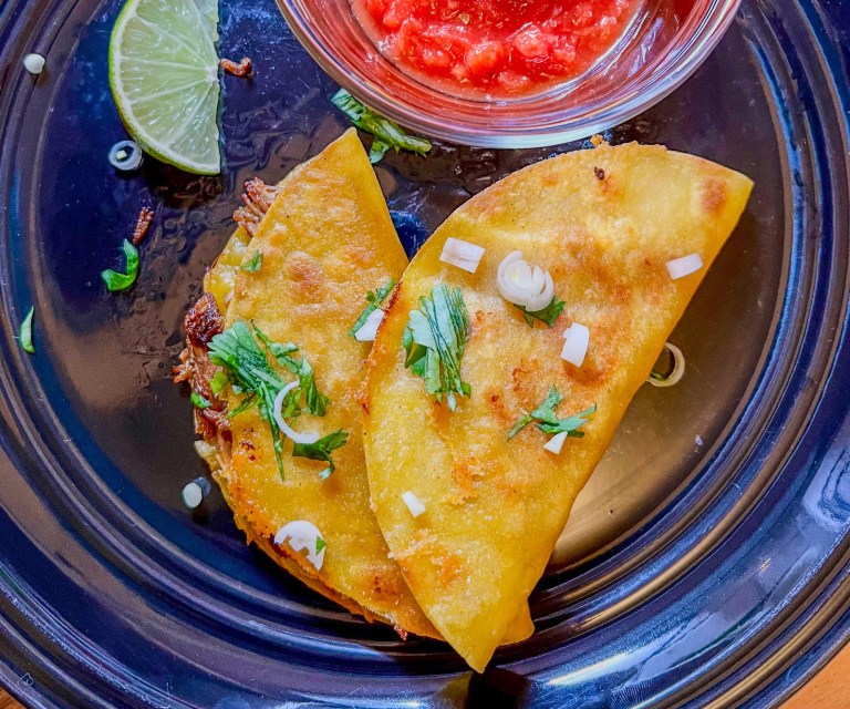 Fried Pulled Pork Tacos on a black plate with a side of salsa