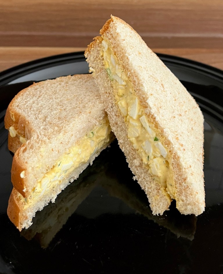 An egg salad sandwich that's been cut in half and sitting on a black plate