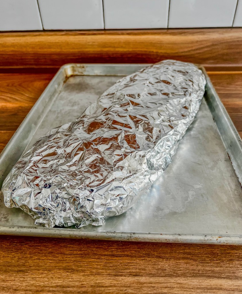 Ribs that have been rubbed and covered in foil on a baking sheet