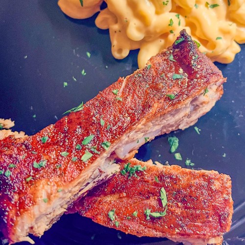 BBQ ribs on a black plate with a side of mac and cheese