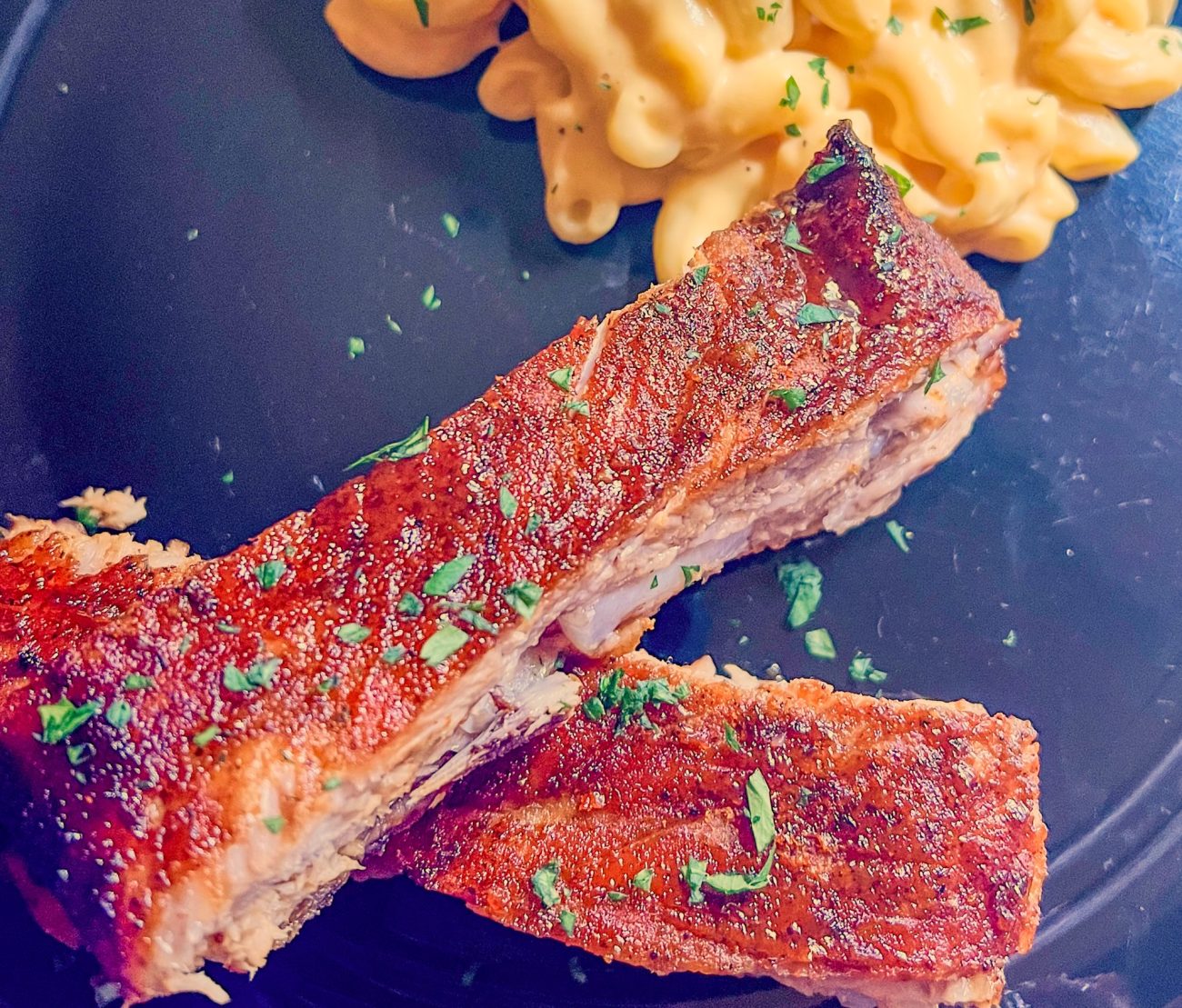 BBQ ribs on a black plate with a side of mac and cheese