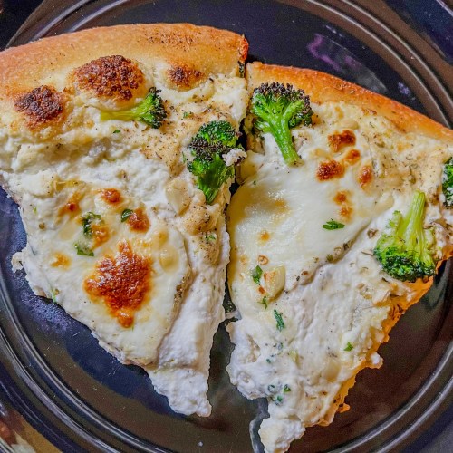 Two slices of white pizza with broccoli on a black plate