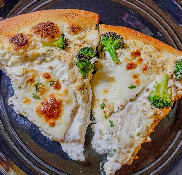 Two slices of white pizza with broccoli on a black plate
