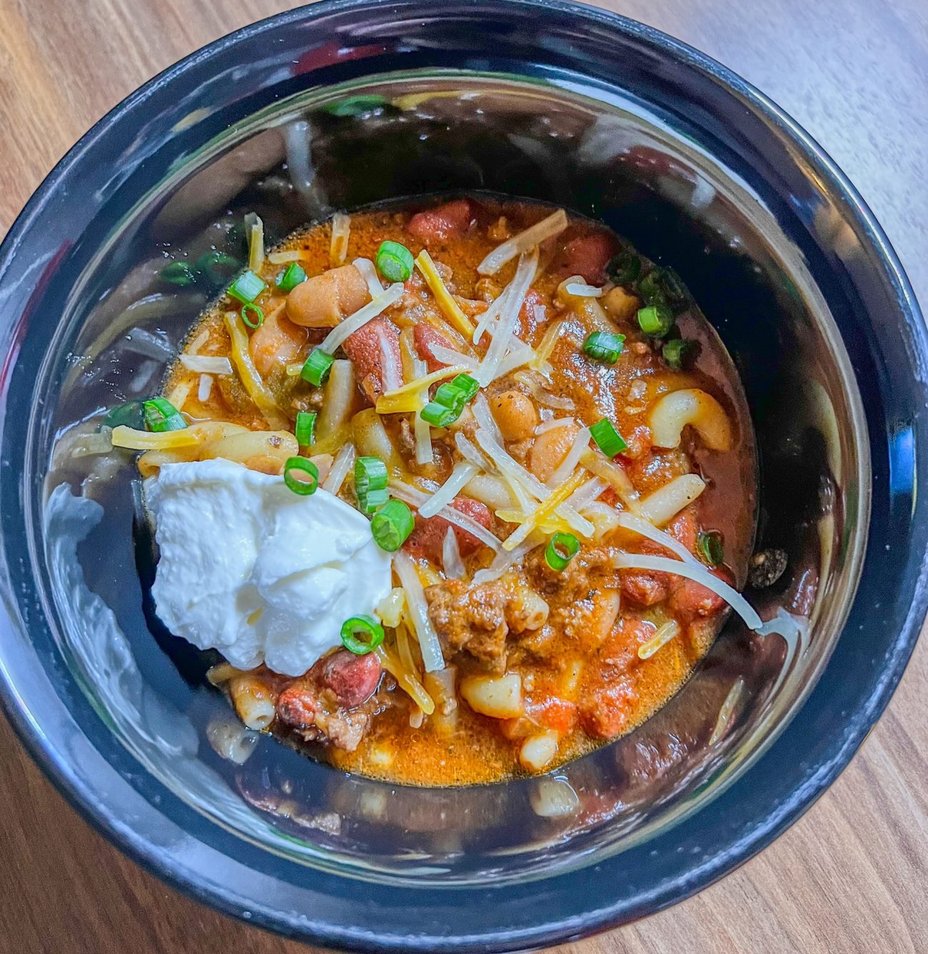 Crockpot chili in a black bowl on a wooden counter