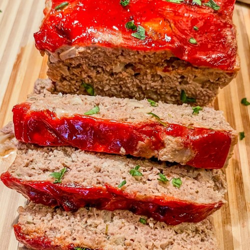 Meatloaf with a ketchup glaze on a wooden cutting board with a knife nearby