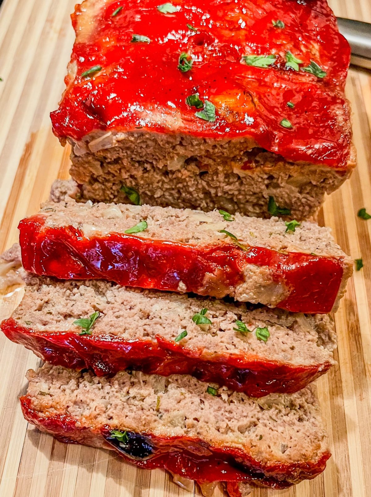 Meatloaf with a ketchup glaze on a wooden cutting board with a knife nearby