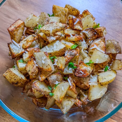 Air fried seasoned potatoes in a large glass bowl on a wooden counter
