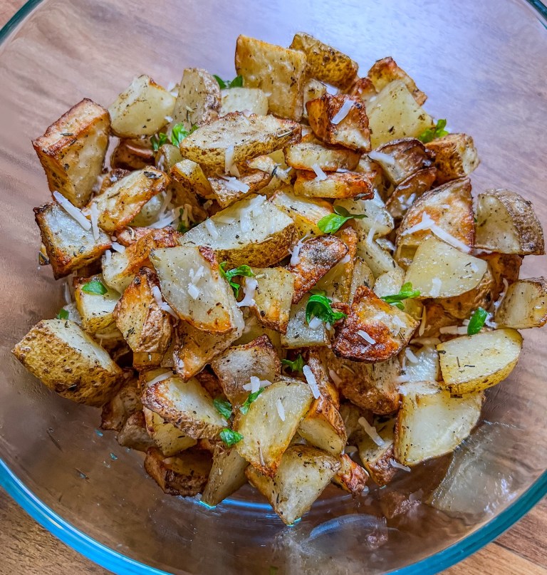 Air fried seasoned potatoes in a large glass bowl on a wooden counter