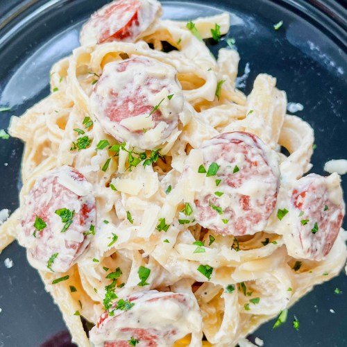 Garlic Sausage Alfredo on a black plate on a wooden table