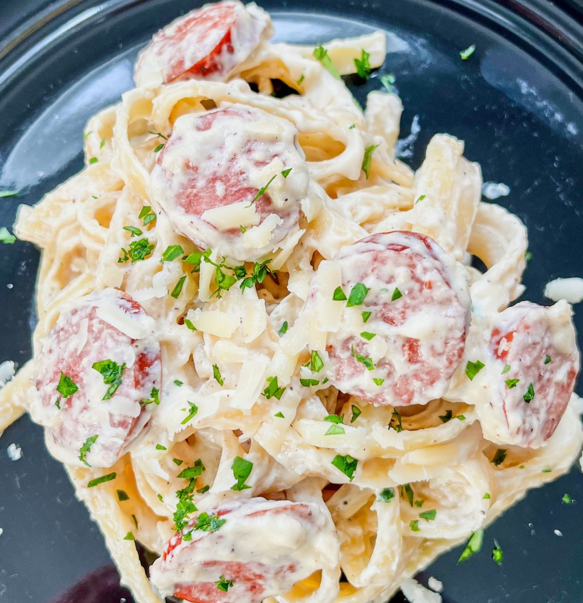 Garlic Sausage Alfredo on a black plate on a wooden table