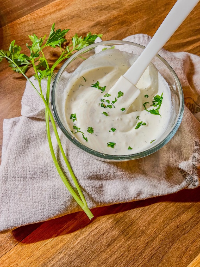 Creamy garlic dressing in a small dish with some parsley lying next to it