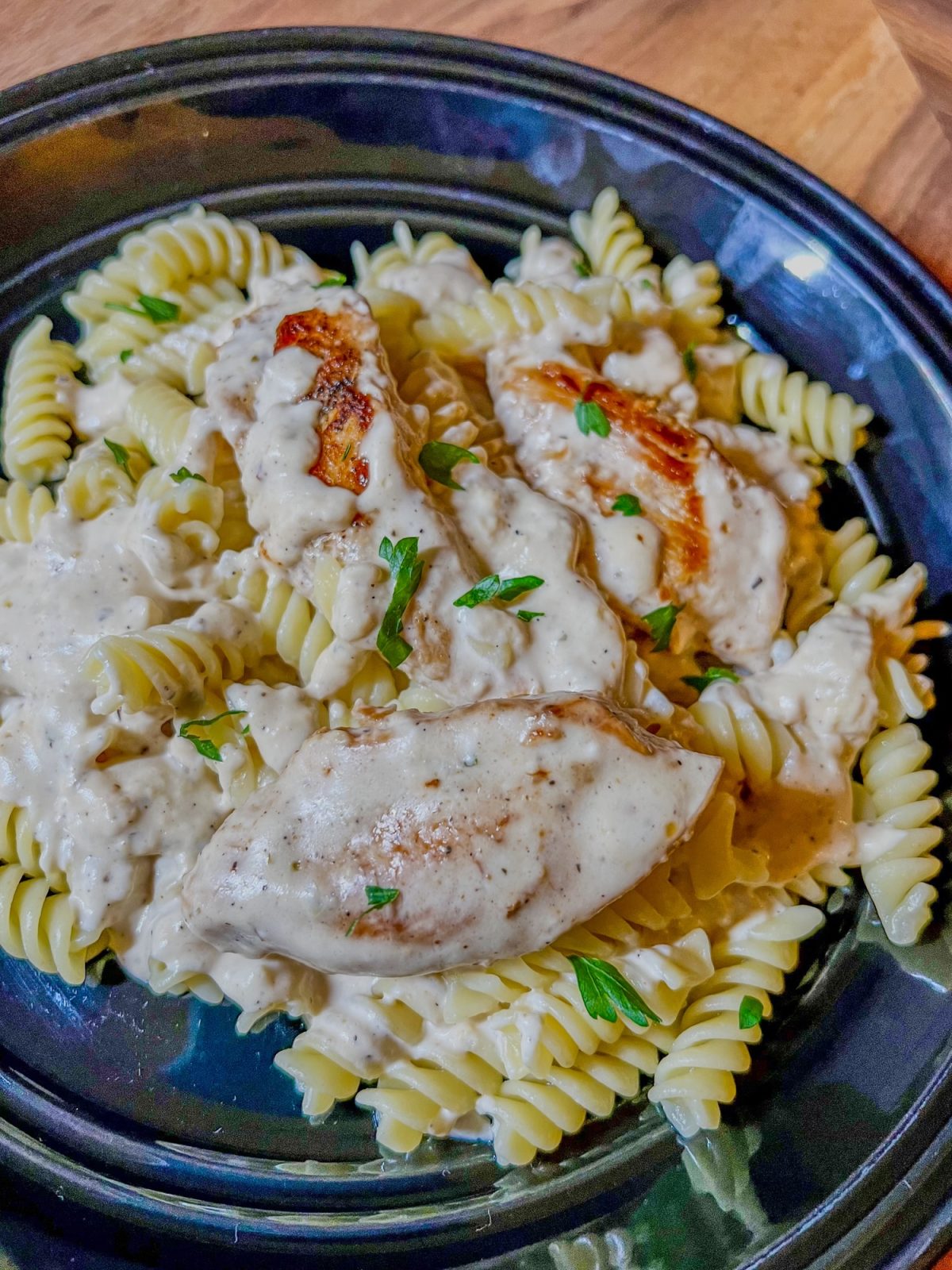 Creamy mustard chicken and pasta on a black plate on a wooden countertop