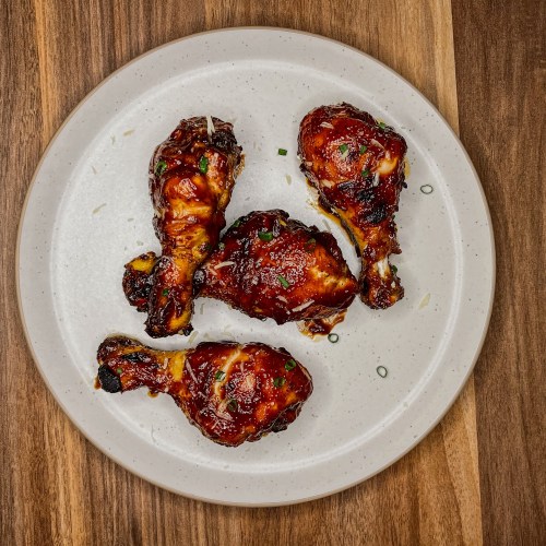 BBQ chicken drumsticks on a white plate on a wooden counter