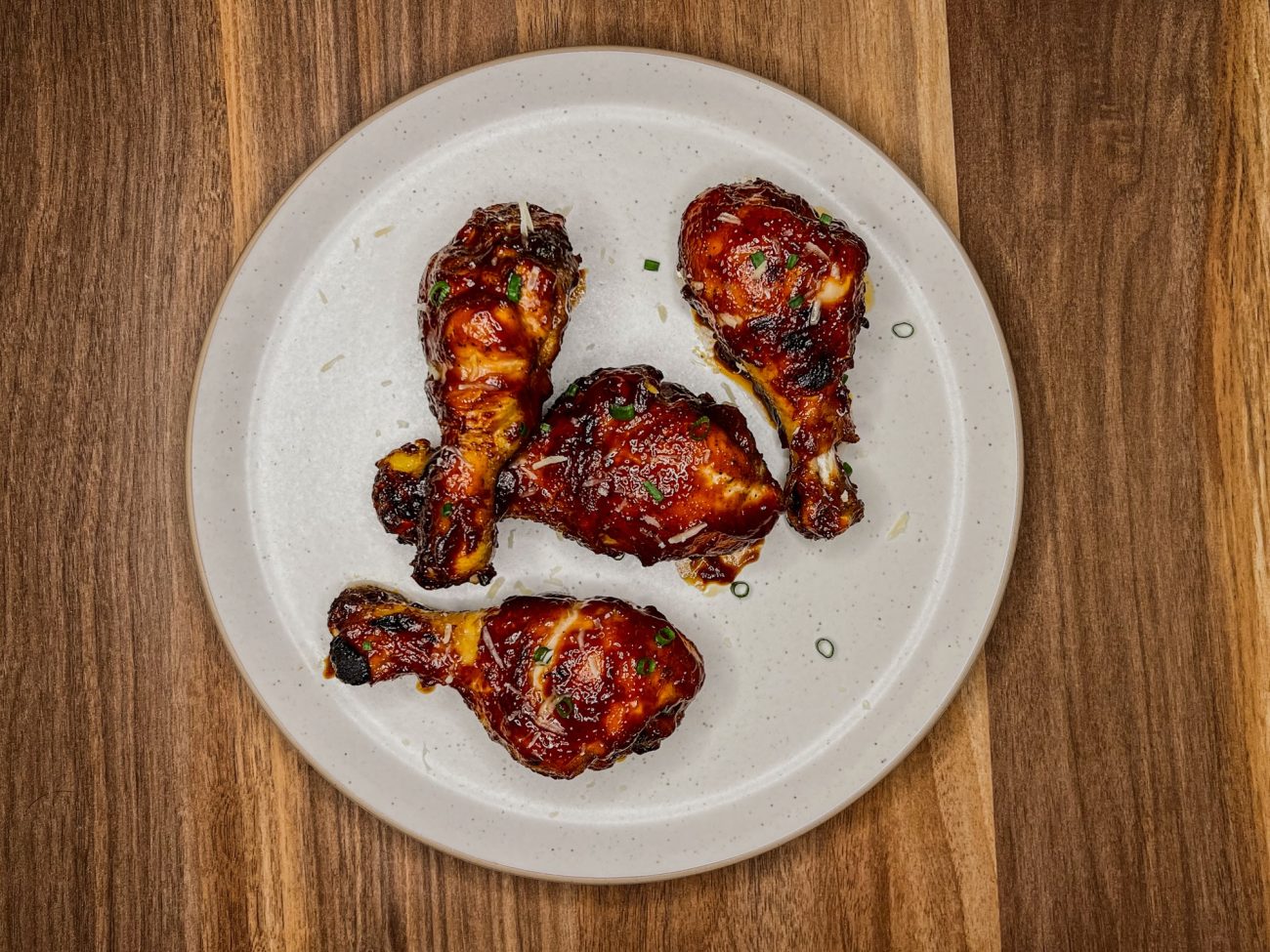 BBQ chicken drumsticks on a white plate on a wooden counter