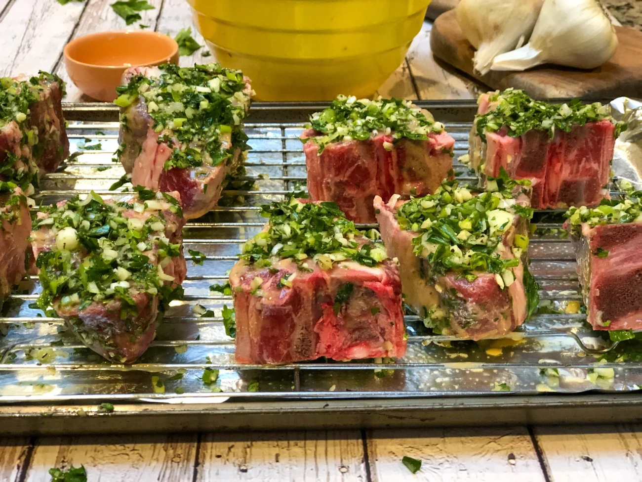 Mediterranean lamb chops with fresh garnishes sitting on a rack over a baking sheet