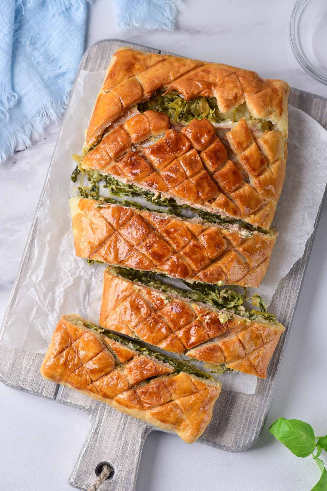 Salmon wellington on a cutting board with fresh herbs scattered around