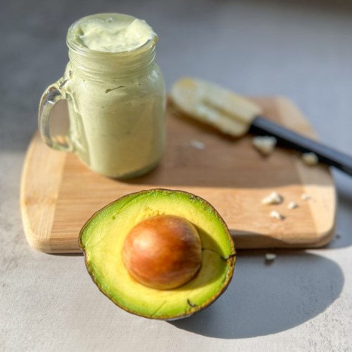 Avocado Blue Cheese Dressing in a glass dish with an avocado and rubber spatula nearby