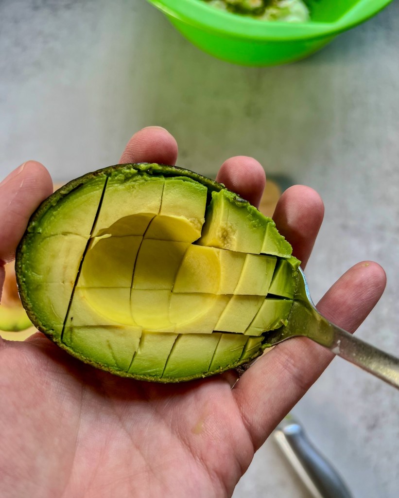 Half of an avocado cut into cubes, getting scooped out with a spoon
