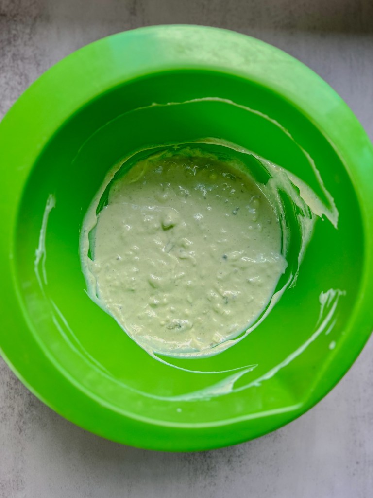 A green bowl filled with avocado blue cheese dressing that's been mixed well