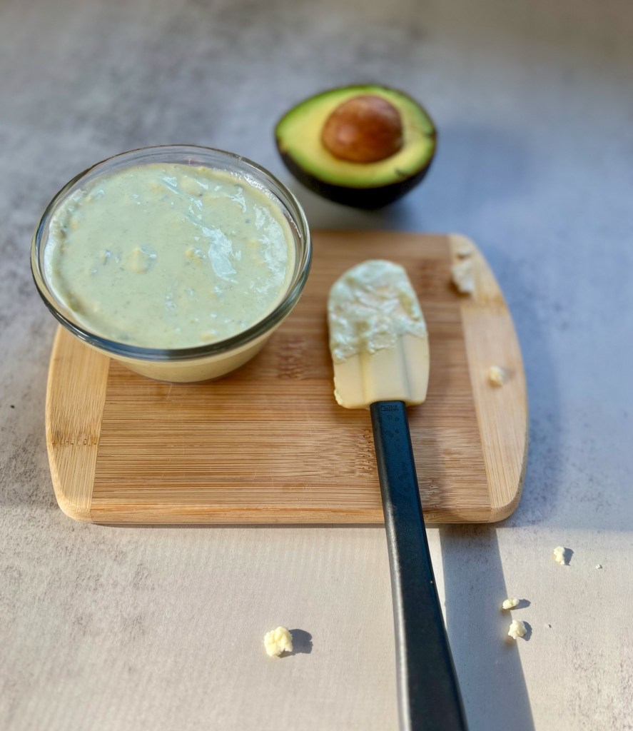 Avocado blue cheese dressing in a dish on a cutting board with an avocado and rubber spatula nearby