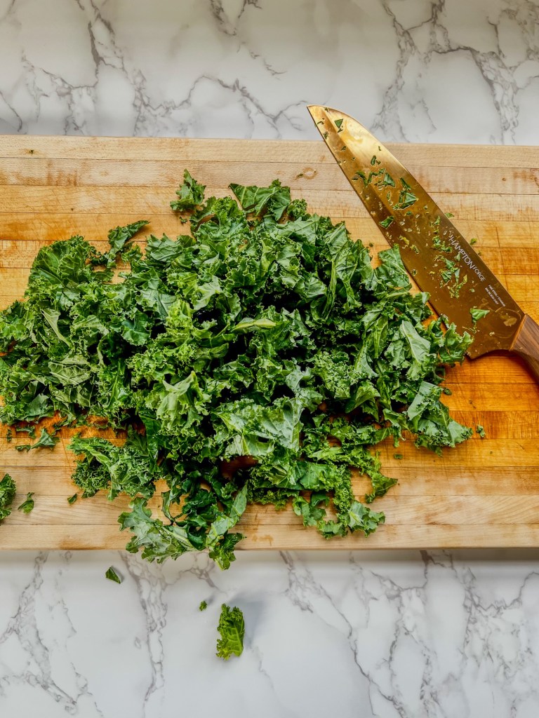 A bunch of kale chopped up on a wooden cutting board with a knife nearby