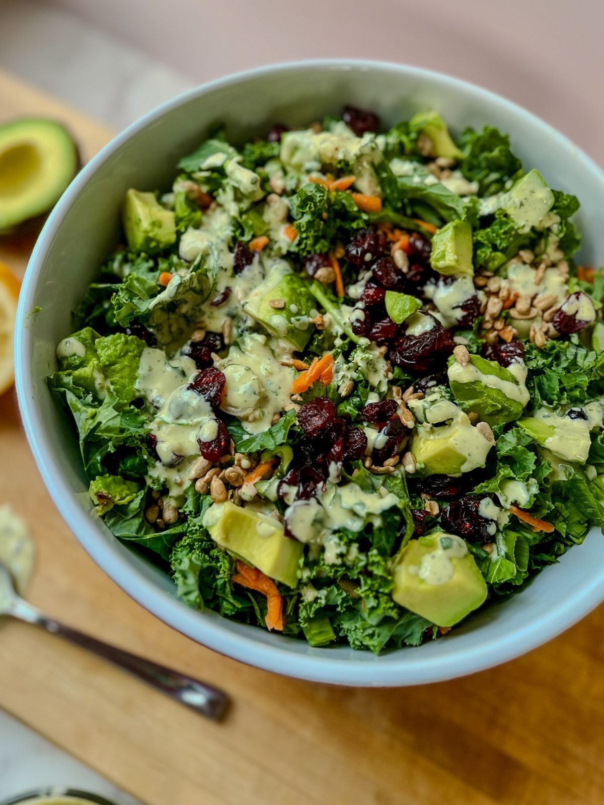 Avocado kale salad in a large bowl on a wooden cutting board with some veggies nearby