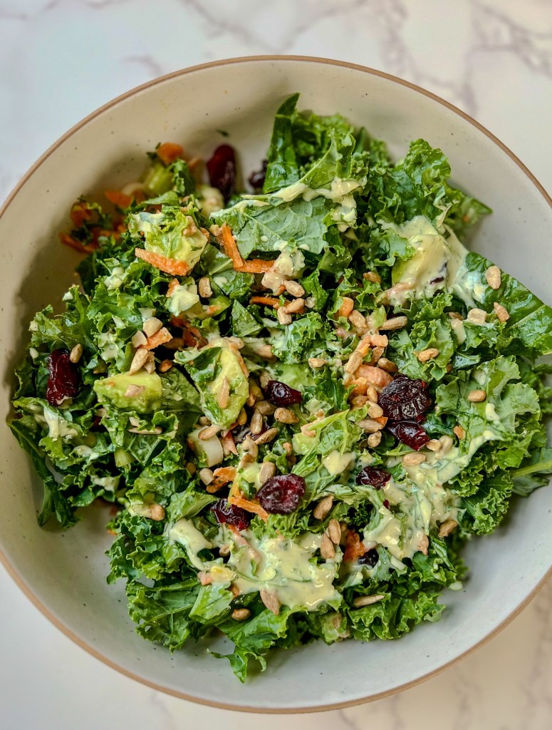 Avocado kale salad in a white bowl on a marble counter