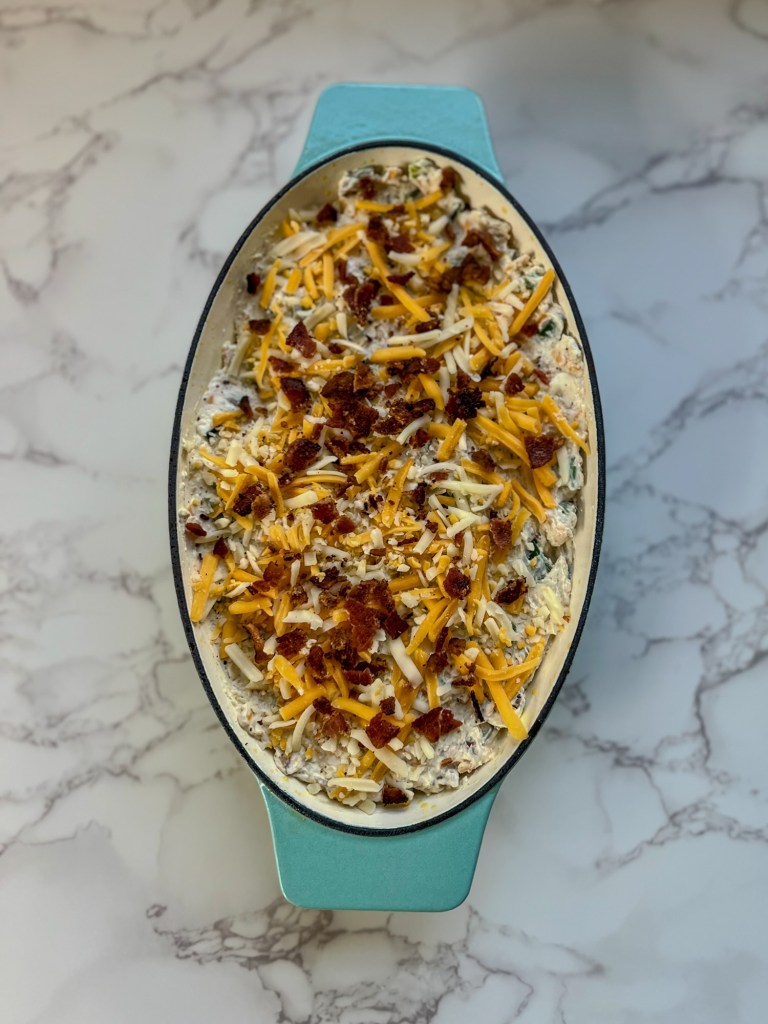 Bacon jalapeño popper dip in a glass dish with bacon and cheese garnished and ready to be baked