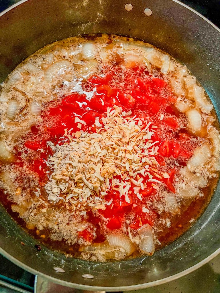 A large skillet filled with onion, tomato, garlic, broth, onion soup mix, and seasonings