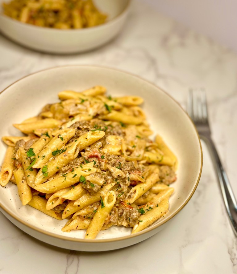 Beefy French Onion Pasta in a white bowl with a fork next to it on a marble counter