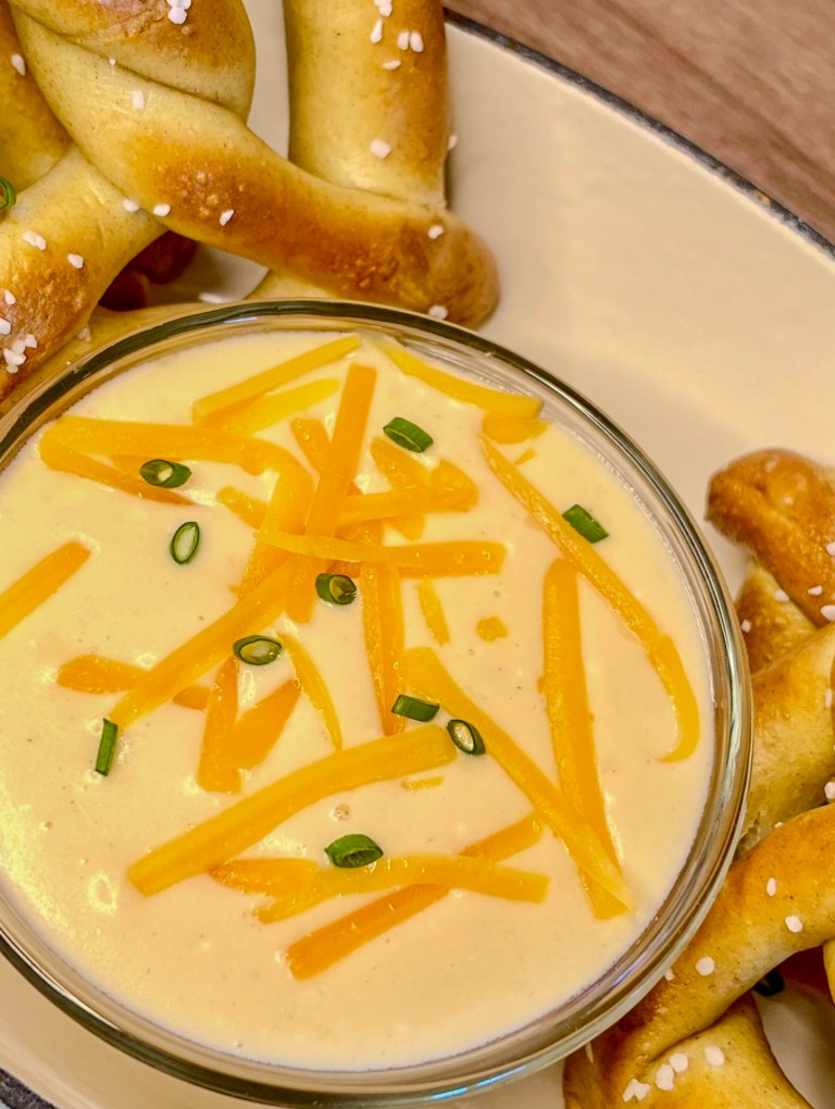Beer cheese served with some pretzels in a serving dish on a wooden counter