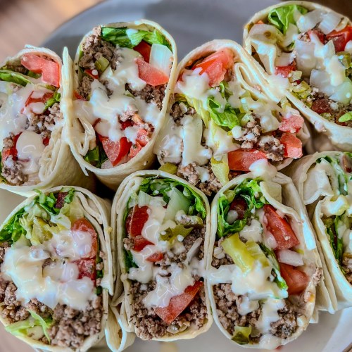 Beer cheeseburger wraps sliced in half on a white plate on a wooden countertop
