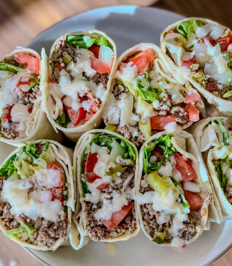 Beer cheeseburger wraps sliced in half on a white plate on a wooden countertop