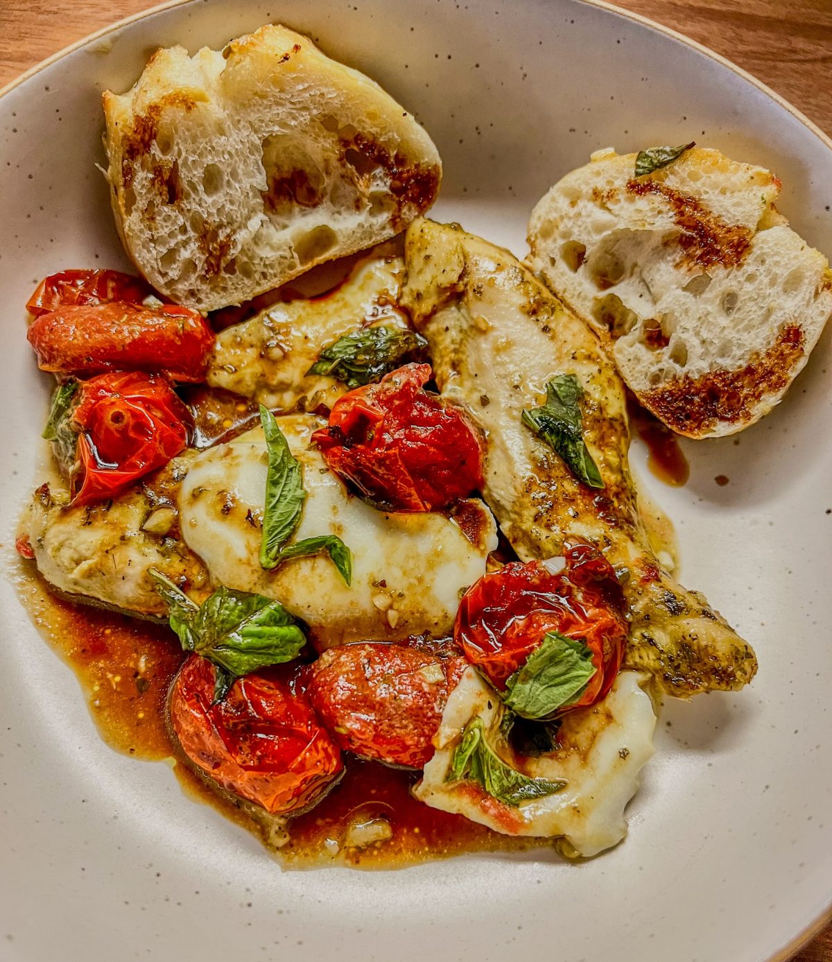 Caprese Chicken Sheet Pan recipe in a white bowl with some bread on the side and balsamic drizzle on top