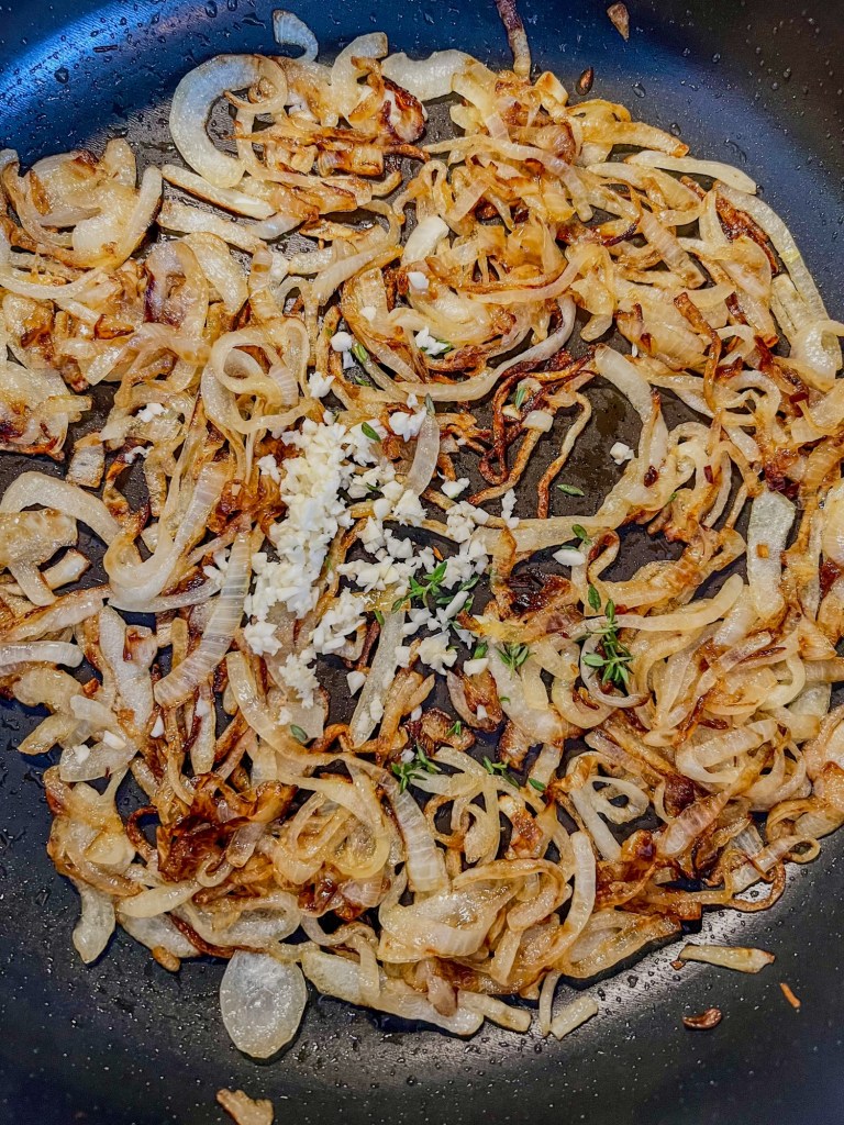 Onions, garlic, herbs, white wine vinegar, butter, and oil cooking in a skillet for french onion dip